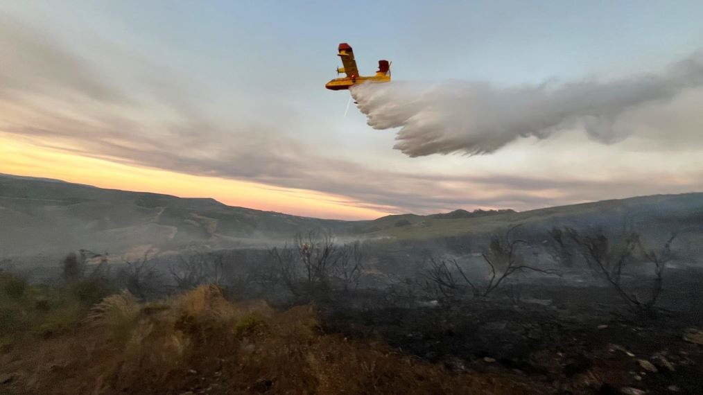 Unha avioneta contraincendios realiza unha descarga sobre o terreo calcinado na Gudiña. (Foto @AT_Brif)